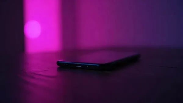 Smartphone sobre una mesa de madera oscura, rodeado de reflejos violetas y rosas (ilustración del artículo)